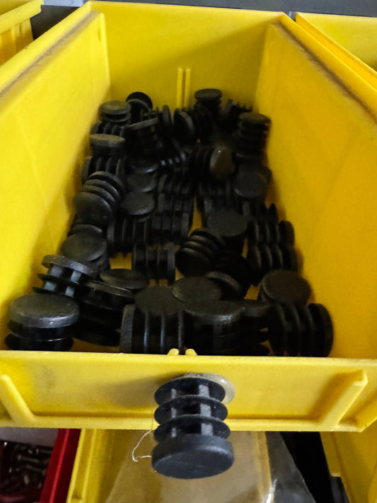 Assorted black plastic push-in tube end caps in a yellow bin